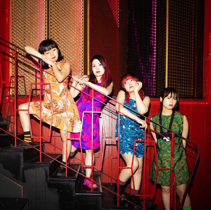 A photo for the Japanese punk band Otoboke Beaver shows them standing in a line on a staircase with each member in a bright colourful dress.