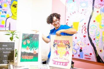 Image of a volunteer holding up two different posters from Sled Island 2022.