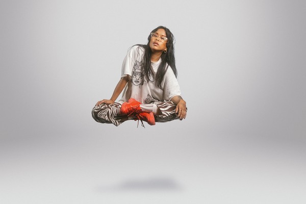 Solo artist Kimmortal is levitating, with legs crossed, in front of a blank background.
