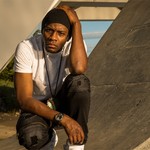 Outdoor portrait of rapper Arlo Maverick, crouched on a cement slope, looking toward the camera.