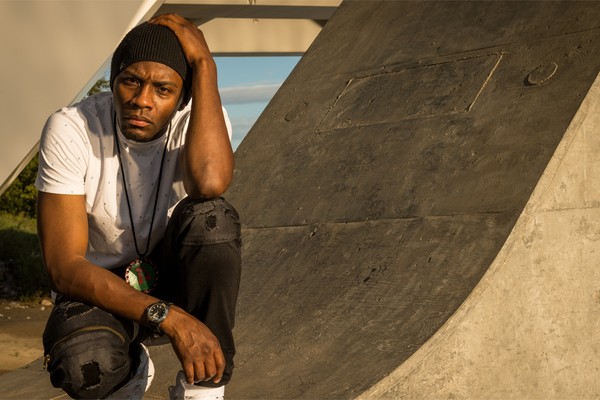 Outdoor portrait of rapper Arlo Maverick, crouched on a cement slope, looking toward the camera.