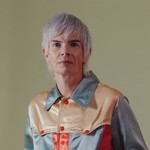 Indoor portrait of solo artist Rae Spoon, looking toward the camera in front of a neutral background.