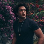 Portrait of solo artist Makaya McCraven gazing over his shoulder with blooming shrubs in the background