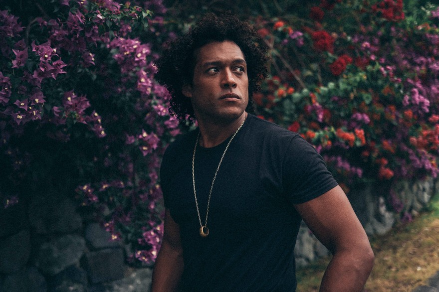 Portrait of solo artist Makaya McCraven gazing over his shoulder with blooming shrubs in the background