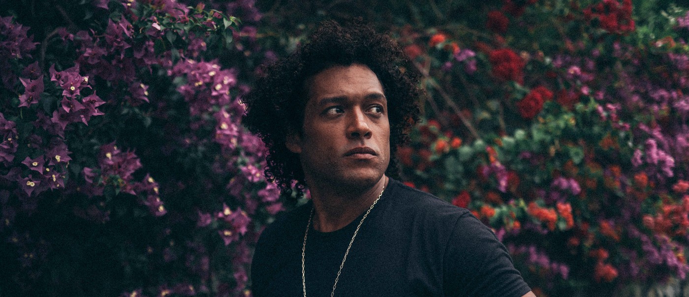Portrait of solo artist Makaya McCraven gazing over his shoulder with blooming shrubs in the background