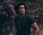 Portrait of solo artist Makaya McCraven gazing over his shoulder with blooming shrubs in the background