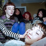 Indoor portrait of five-piece PERRA. Members are interacting with one another candidly, in a home setting with three members seated on a couch and one member stroking the face of another.