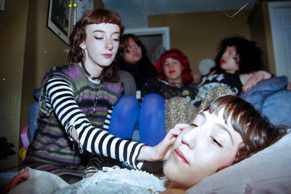 Indoor portrait of five-piece PERRA. Members are interacting with one another candidly, in a home setting with three members seated on a couch and one member stroking the face of another.