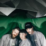 Studio portrait of trio Motherhood posed closely together with a dark mesh covering them