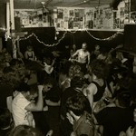 A black and white photo shows the band SMUTHER playing a packed intimate show, standing in the corner of a small room. 