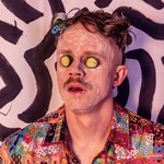 Zany portrait of Taylor Cochrane of 36? with cucumbers on his eyes staring blankly with clay spread on his face.
