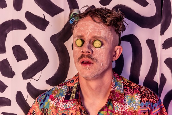 Zany portrait of Taylor Cochrane of 36? with cucumbers on his eyes staring blankly with clay spread on his face.