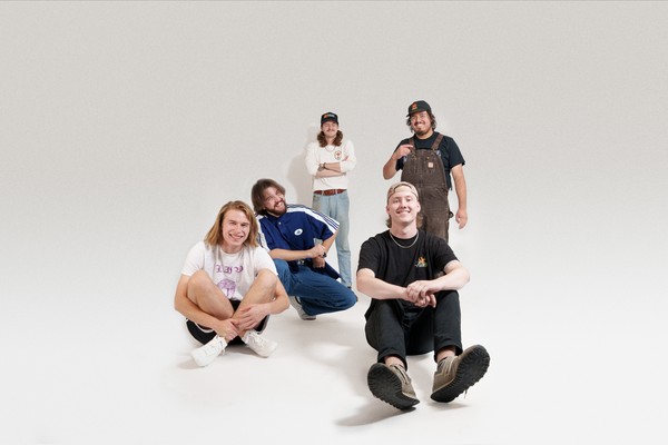 Studio portrait of five-piece 4BPM. Three members are seated and two are standing, all smiling toward the camera.