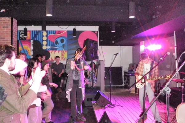 Photo of act ADOPTION peforming with a guitar on stage, in front of an engaged audience.