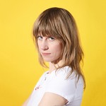 Portrait of solo artist Amery looking toward the camera, in front of a yellow backdrop.