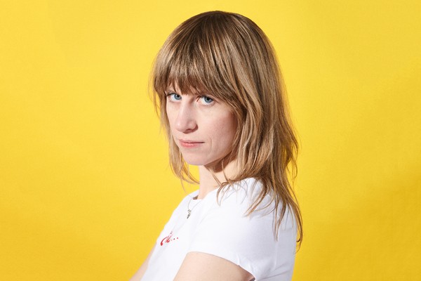 Portrait of solo artist Amery looking toward the camera, in front of a yellow backdrop.