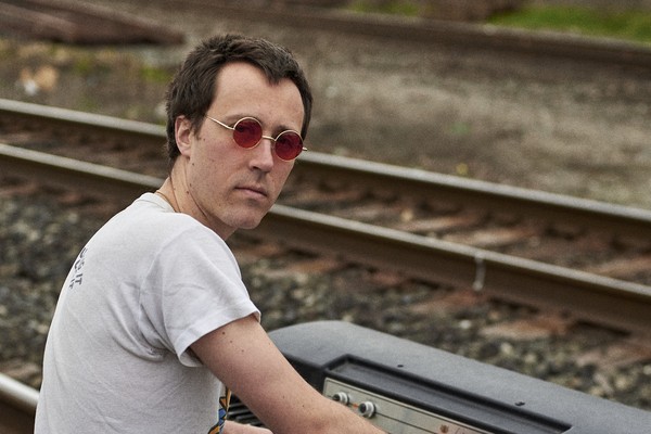 Avalon Tassonyi is playing an antique keyboard on a traintrack, looking toward the camera