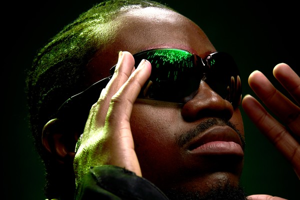 Close up portrait of rapper Banggz in dark sunglasses, looking to the side with his hands on each side of his face.