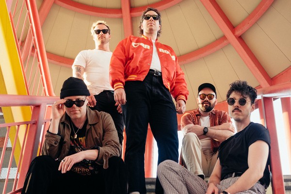 Taken from below, five-piece BETABOYS are posed on a covered set of outdoor stairs, each looking toward the camera