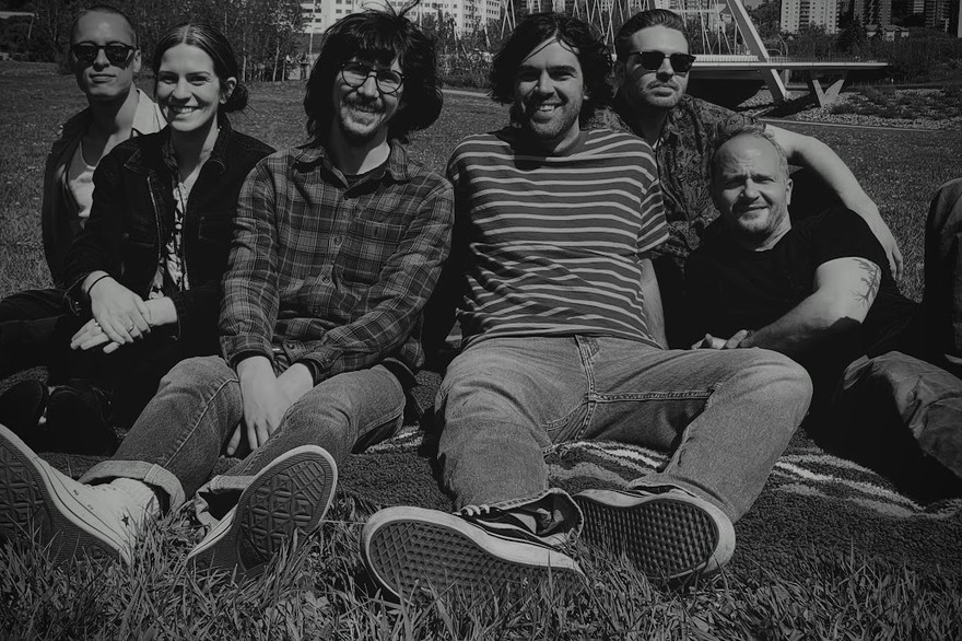 Black and white image of six-piece Big Evil Rat all sitting on a towel in a grassy inner-city park and smiling toward the camera.