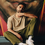 Solo artist Bijaan is sitting against a large outdoor street painting.
