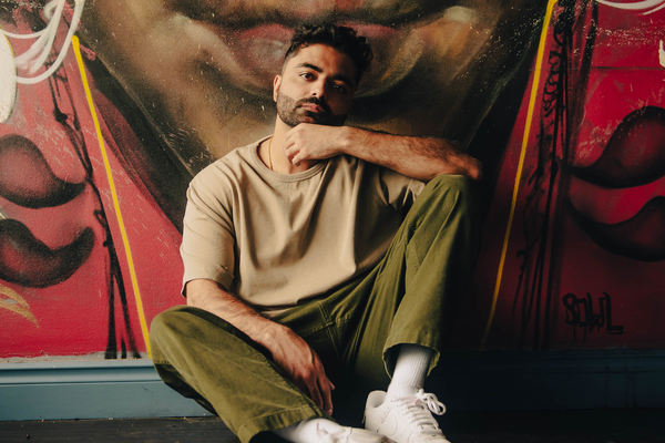 Solo artist Bijaan is sitting against a large outdoor street painting.