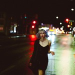 Photo taken at night of Michele ii Visser of Boniface walking down a major road with streetlights and carlights lighting the background.