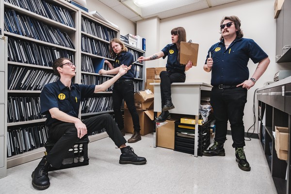 Photo taken in an office of four-piece Brain Bent interacting with one another while holding office items.