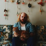 Photo of Carter Felker sitting on a floral couch and holding an orange cat.