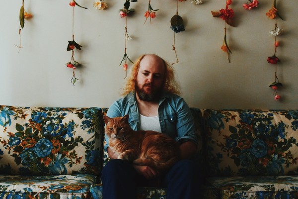 Photo of Carter Felker sitting on a floral couch and holding an orange cat.