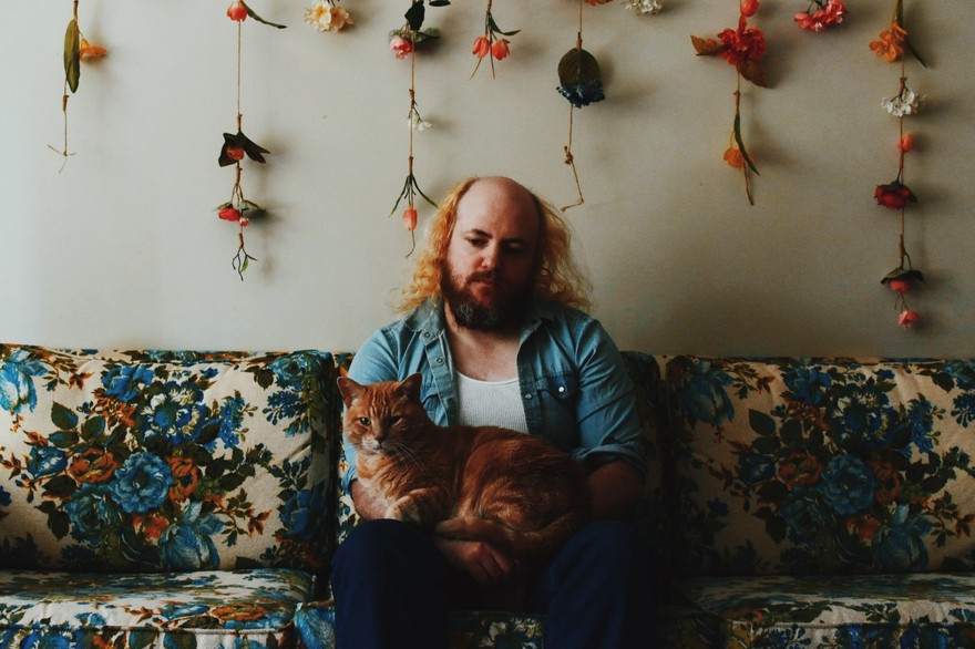 Photo of Carter Felker sitting on a floral couch and holding an orange cat.
