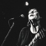 Captured in motion, black and white photo of Cassia Hardy performing on stage with a guitar.