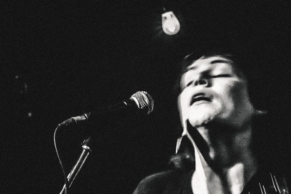 Captured in motion, black and white photo of Cassia Hardy performing on stage with a guitar.