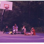 Photo of four members of cootie catcher sitting on an outdoor basketball court
