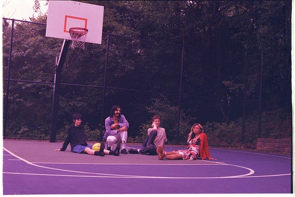 Photo of four members of cootie catcher sitting on an outdoor basketball court