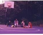Photo of four members of cootie catcher sitting on an outdoor basketball court