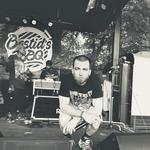 Black and white photo of Daniel Son crouching between two speakers on an outdoor stage.