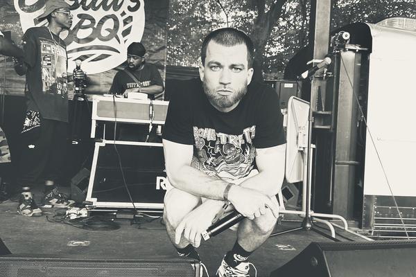 Black and white photo of Daniel Son crouching between two speakers on an outdoor stage.