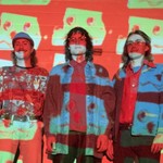 Photo of four members of Dial Up standing against a wall with a projector casting images of a robotic face upon them