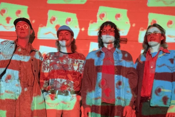 Photo of four members of Dial Up standing against a wall with a projector casting images of a robotic face upon them