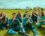 Outdoor photo taken on a field on a sunny day, featuring seven members of DOOM GONG blowing dandelions while dressed in matching denim