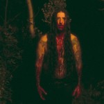 Dark outdoor photo featuring a member of ECHTHROS with long dark hair, covered in blood on their hands, mouth and chest.