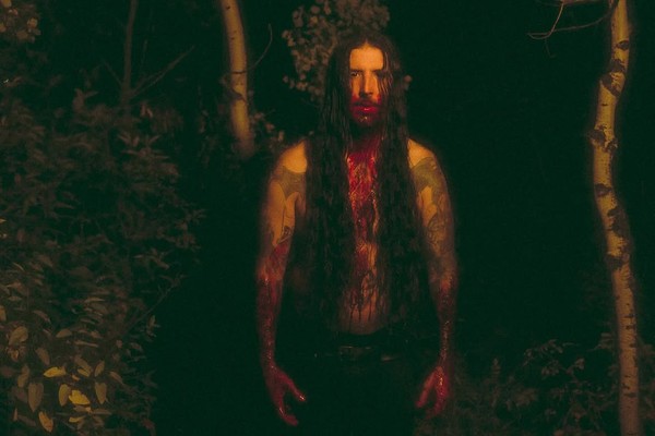 Dark outdoor photo featuring a member of ECHTHROS with long dark hair, covered in blood on their hands, mouth and chest.