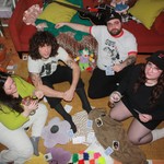 Taken from above, four members of Emma Goldman are playing a game of cards on the the floor of an apartment.