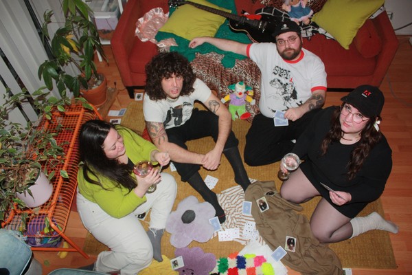 Taken from above, four members of Emma Goldman are playing a game of cards on the the floor of an apartment.