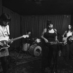 Black and white photo of four-piece Eraser performing on stage with a guitar, bass, keyboard and drums