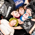 Taken from below, a colour photo shows the five-piece punk band Glitter Glue in a huddle looking down at the camera.
