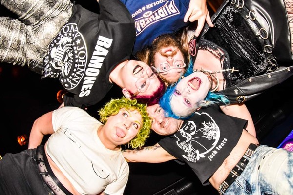 Taken from below, a colour photo shows the five-piece punk band Glitter Glue in a huddle looking down at the camera.