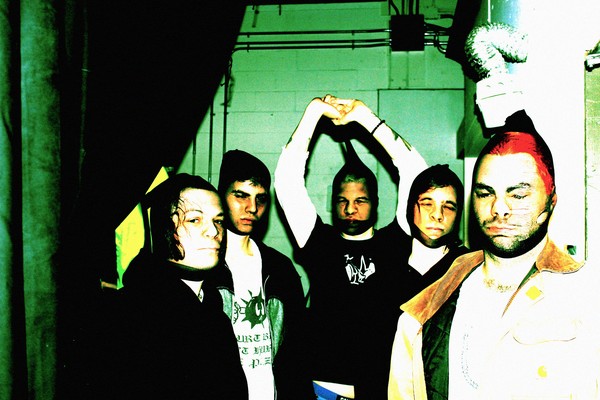 An over exposed colour photo shows the five-piece band Hillboro standing in a room all with pantyhose over their faces.