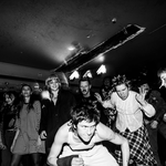 A black and white photo shows artist Jed Arbour crouching in front of an enthusiastic crowd during a live performance.